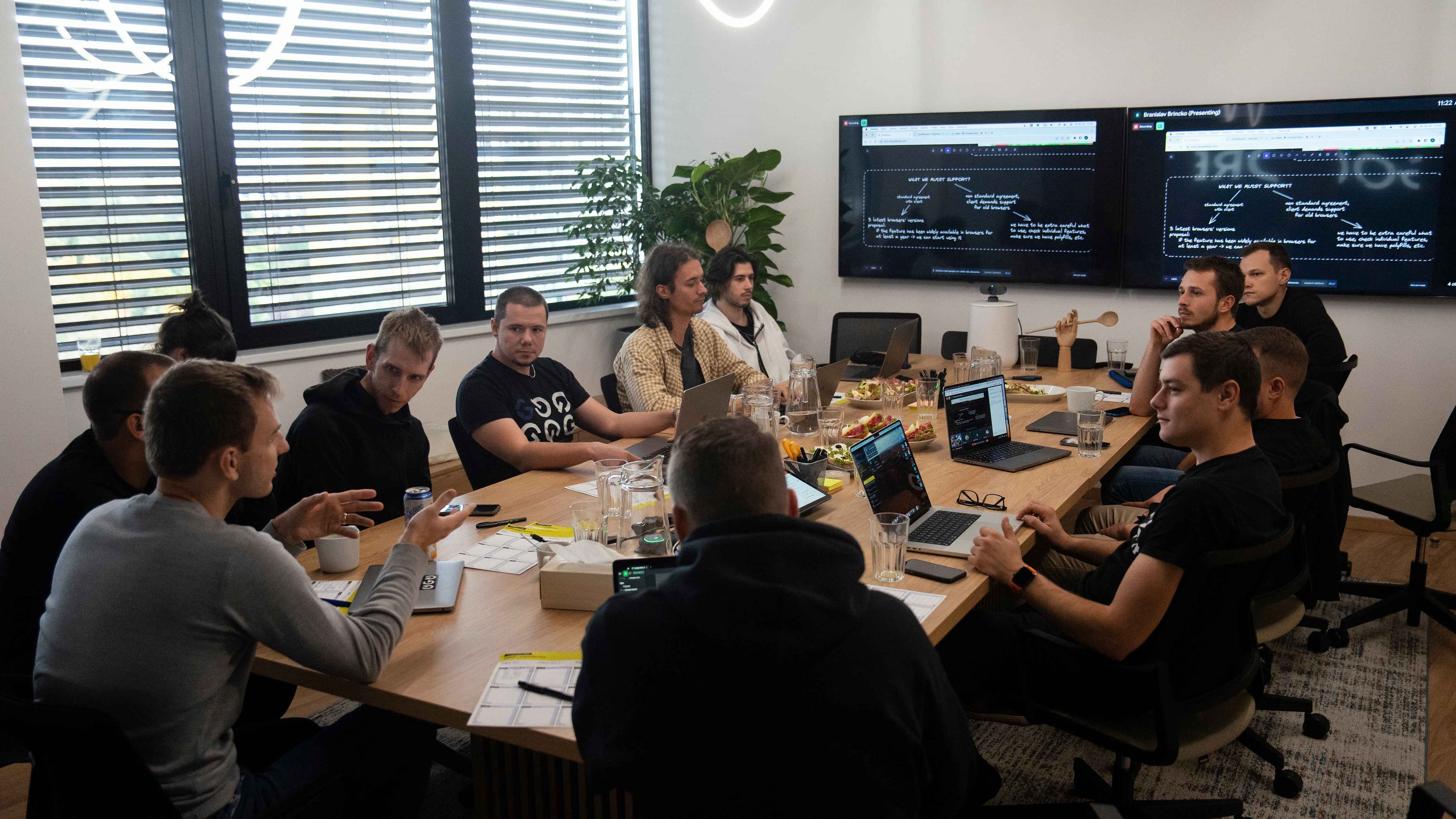 Fotografia viacrých ľudí, sediacich v zasadacej miestnosti, s pohľadom na obrazovky zavesené na stene počas Frontend Days.