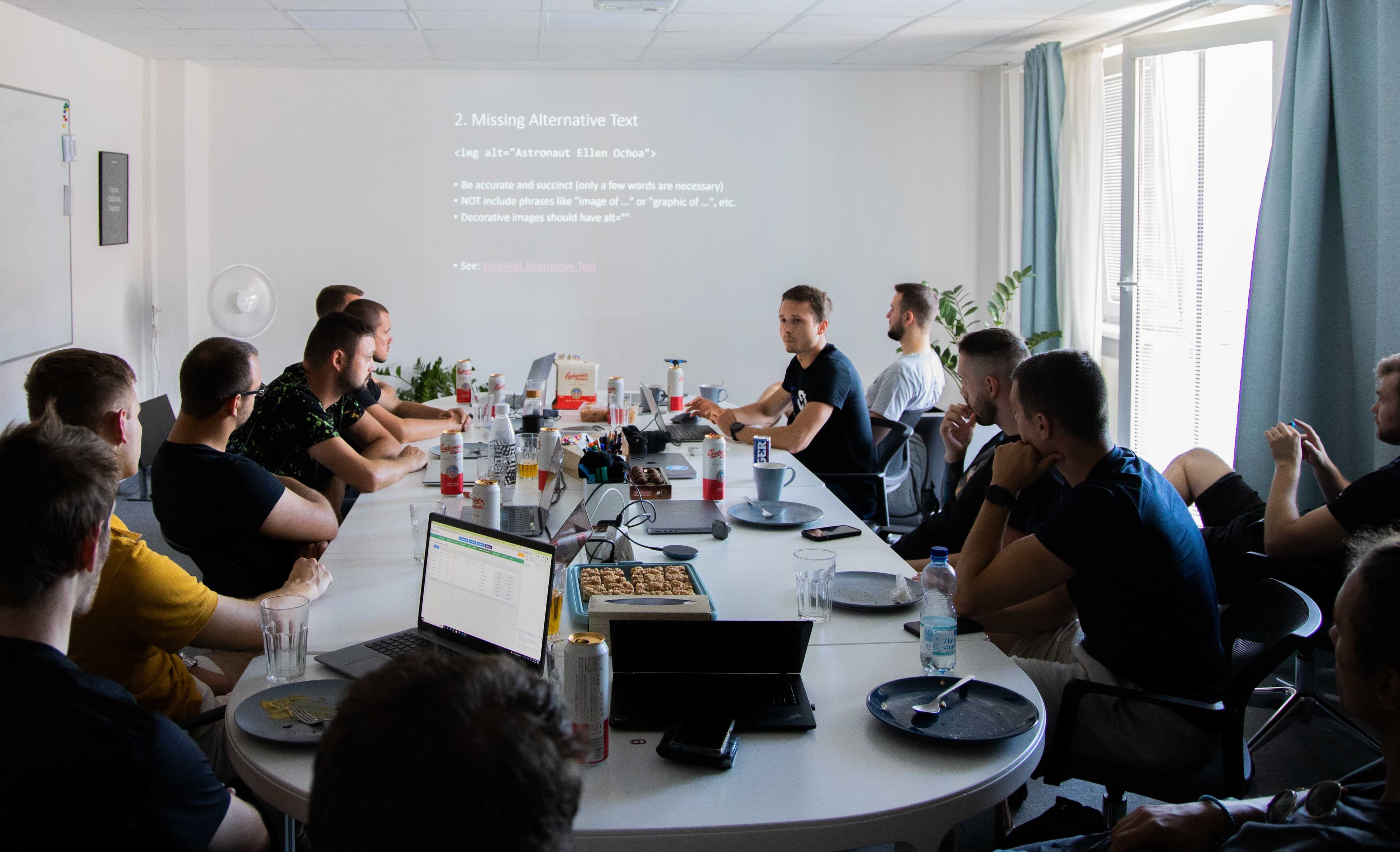 Stretnutie počas Frontend days - konferenčná miestnosť s ovalným stolom, za ktorým sedia viaceré osoby, na stenu pred stolom je vysvietená prezentácia. 