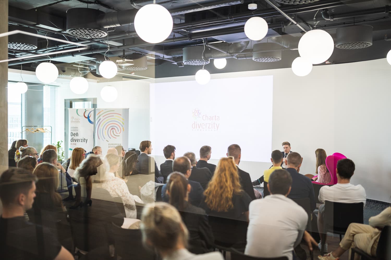 Konferenčná miestnosť s účastníkmi prezentácie. Na plátne je logo Charty diverzity Slovensko, v miestnosti sú bannery k Dňu diverzity 30. mája.
